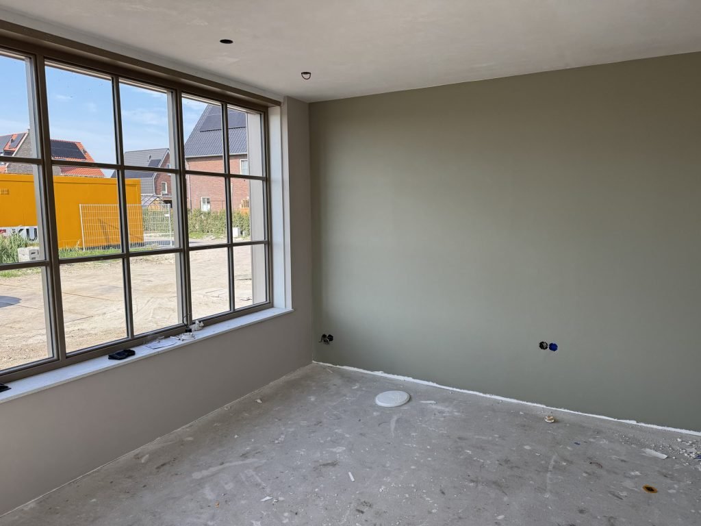Nieuwbouwkamer met een egaal grijsgroen gesausde wand en een groot roedenraam