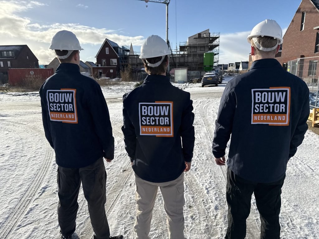 Drie vakmensen van Bouwsector Nederland met witte helm op een besneeuwde nieuwbouwplaats